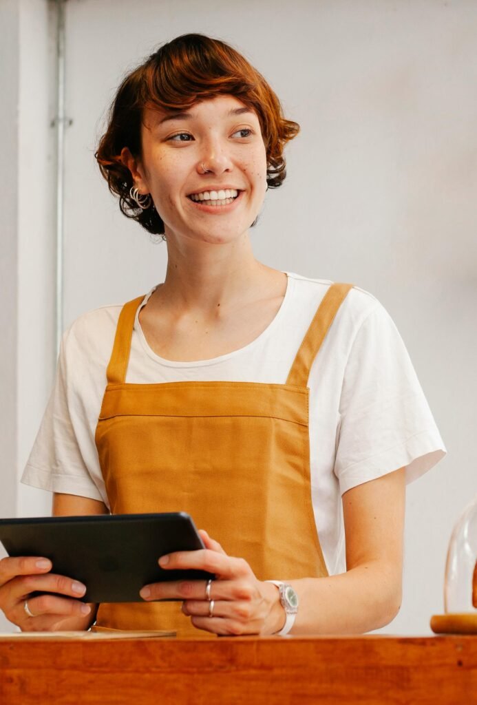 Young glad female employee with tablet looking away at counter in cafeteria in daylight