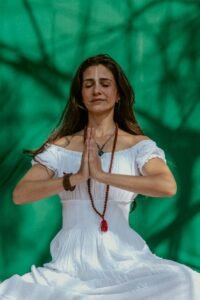 Calm and relaxed woman meditating outdoors with a vibrant green background.