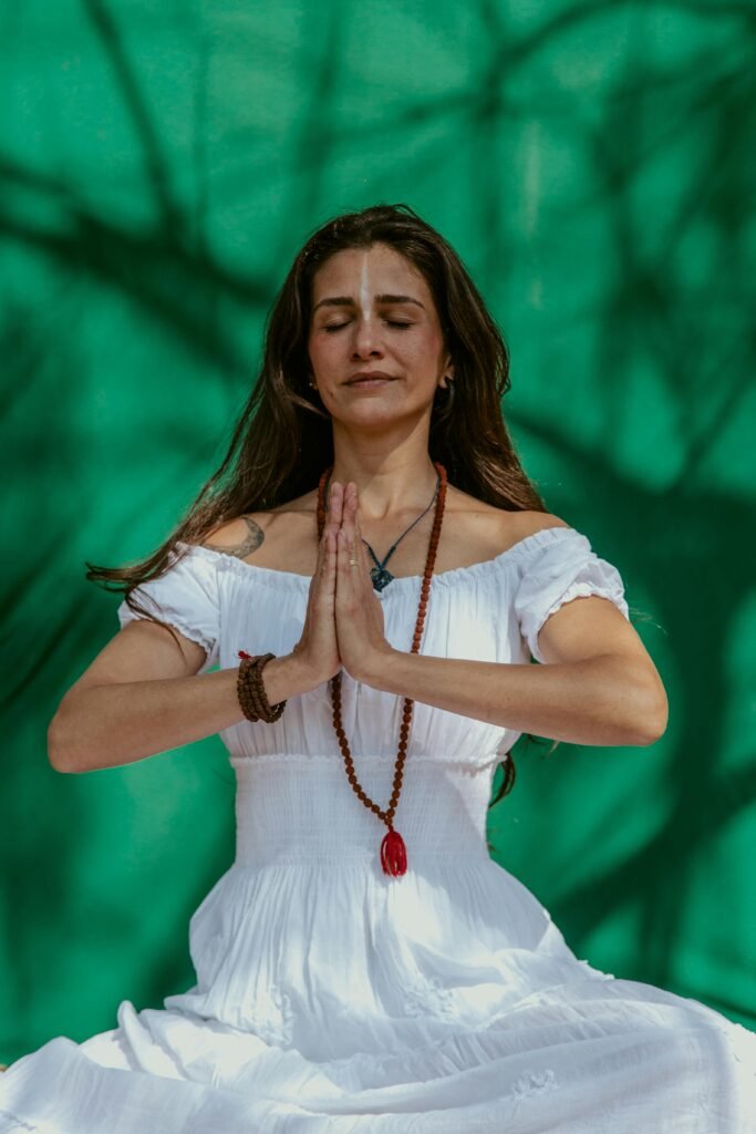 Calm and relaxed woman meditating outdoors with a vibrant green background.