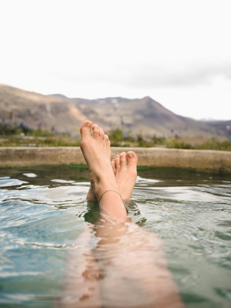 Feet relaxing in a hot spring with a stunning view of Iceland's mountains, perfect for leisure and travel themes.
