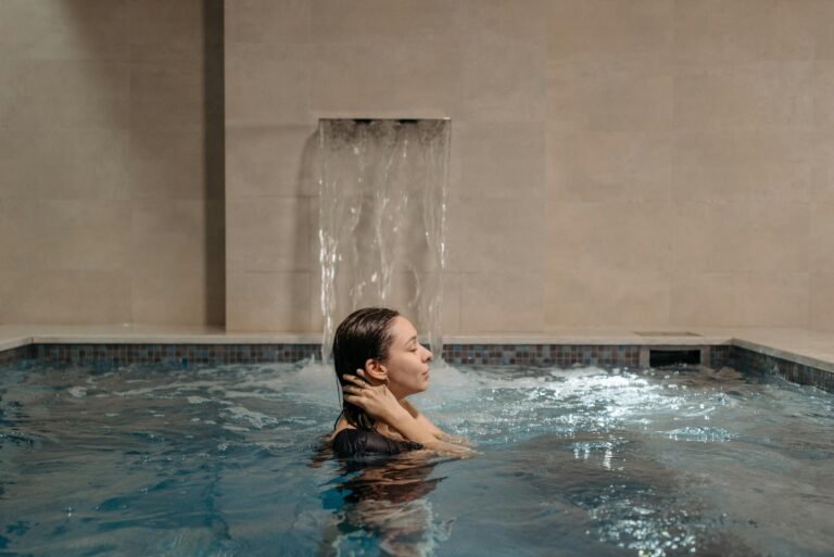 Adult woman relaxing in an indoor swimming pool near a cascading waterfall.