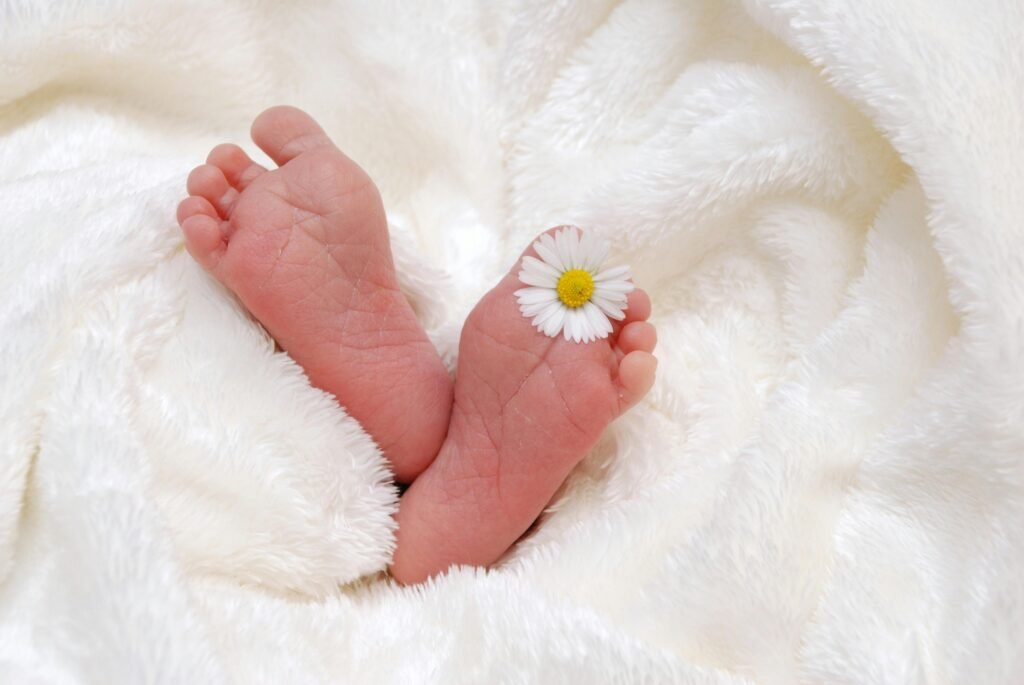 Close-up of newborn feet with a daisy on a fluffy white blanket.