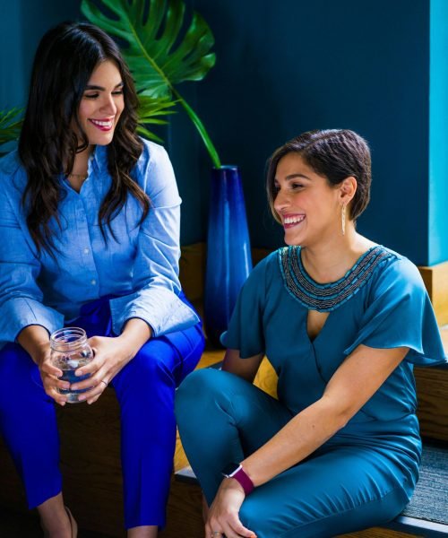 Two women enjoying a lively conversation indoors, showcasing stylish and colorful attire.