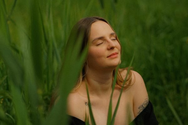 Woman in a Black Dress Sitting in the Grass with Her Eyes Closed