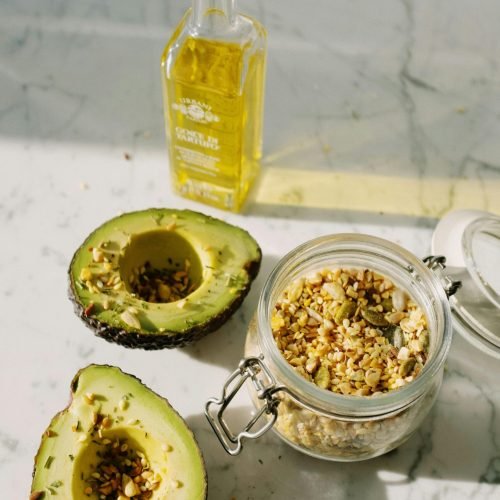 Fresh avocado halves with pine nuts and olive oil on marble surface, highlighting healthy eating.