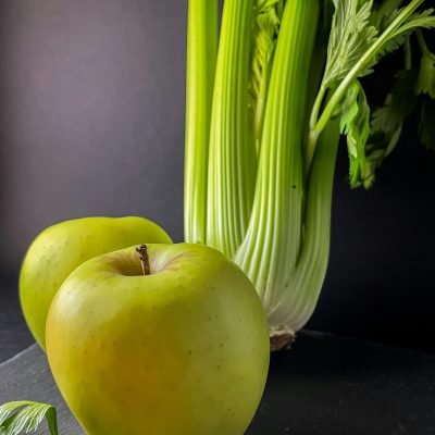 A still life of fresh green apples and celery stalks on a dark surface, emphasizing healthy food.